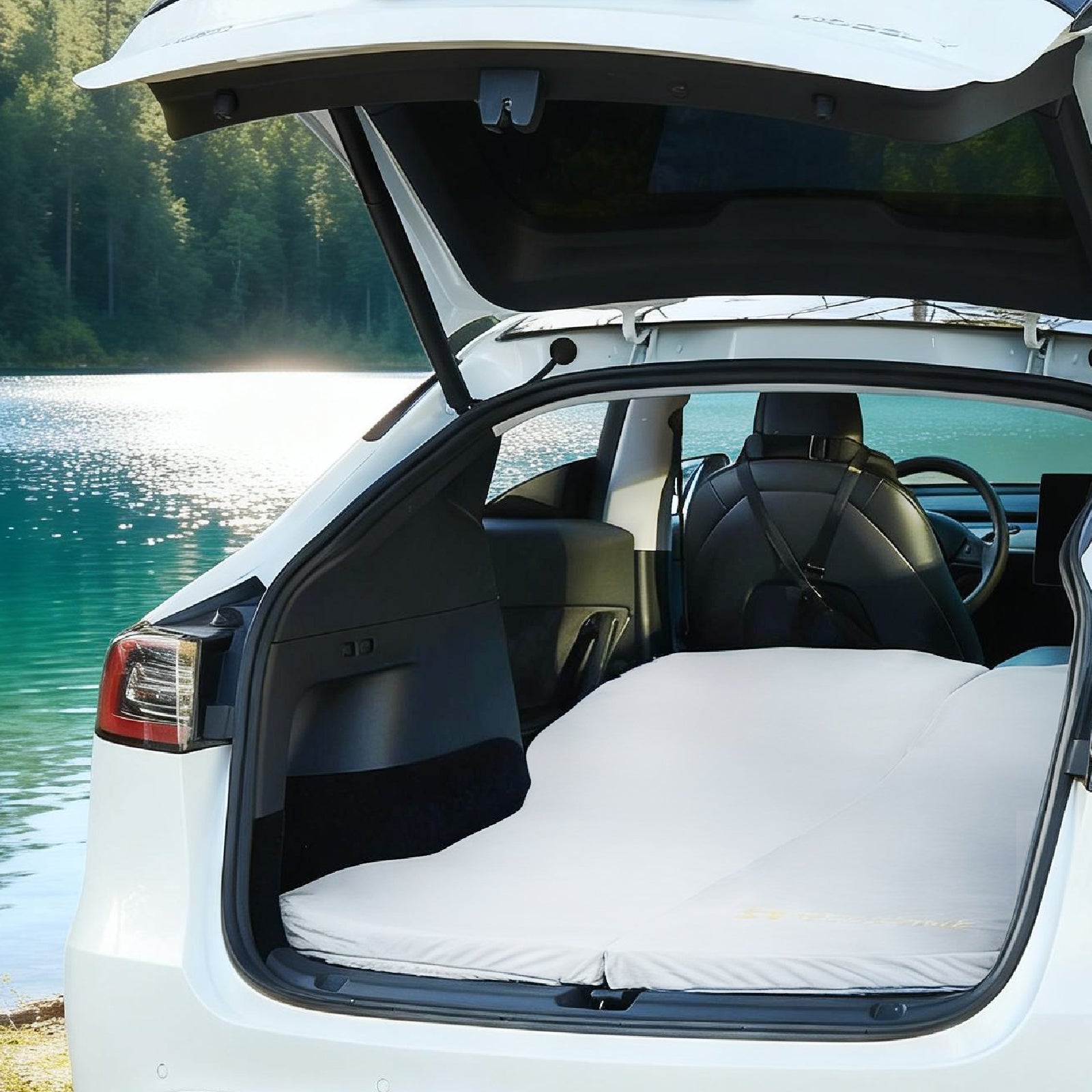 White Tesla Model Y with memory foam camping mattress unfolded in open trunk beside mountain lake