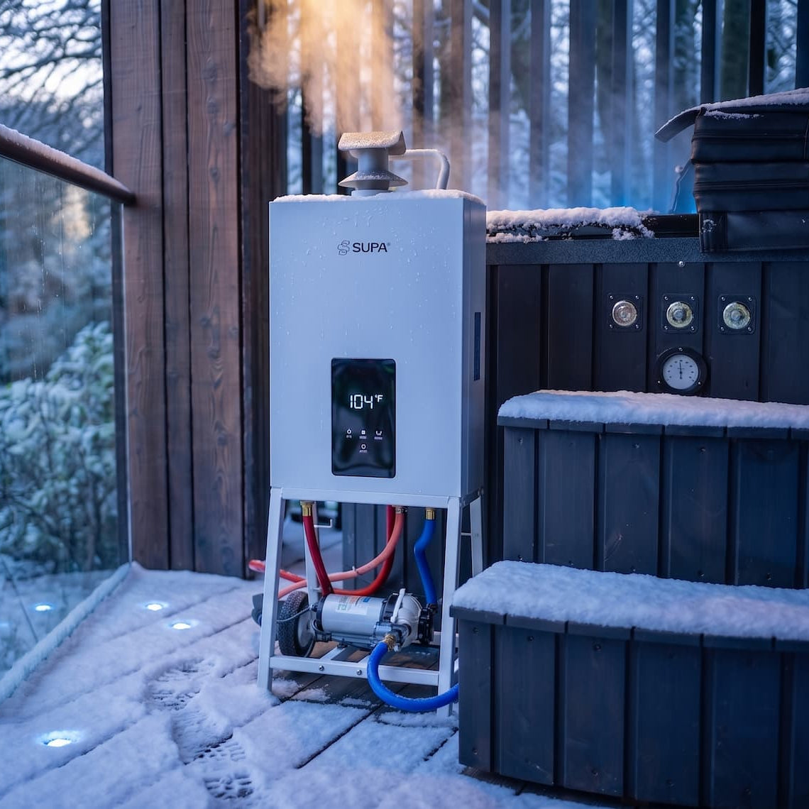 A portable outdoor steam hot tub heater standing on a snowy wooden deck next to a dark hot tub, with visible steam rising and winter trees in the background.