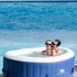 Two people in a blue inflatable hot tub by a pool.